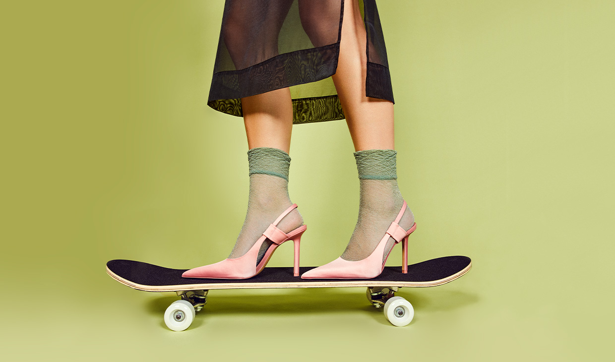 Fødder i stiletter på et skateboard med grøn baggrund